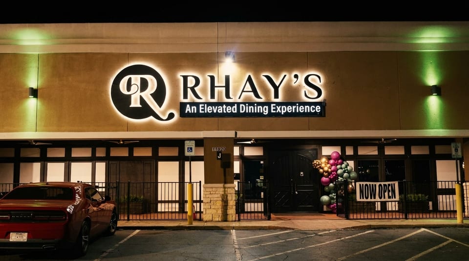 Exterior of Rhay's restaurant at night, with a red car parked in front and a "Now Open" sign.